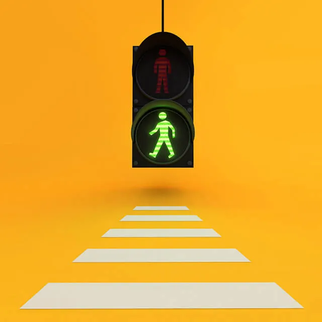 On a flat orange ground, a black pedestrian traffic light hangs on a thin cable. Its upper lens shows a red standing figure, its lower lens a glowing green walking figure. Five white paper stripes lie on the ground below in steep perspective, running away from the viewer.