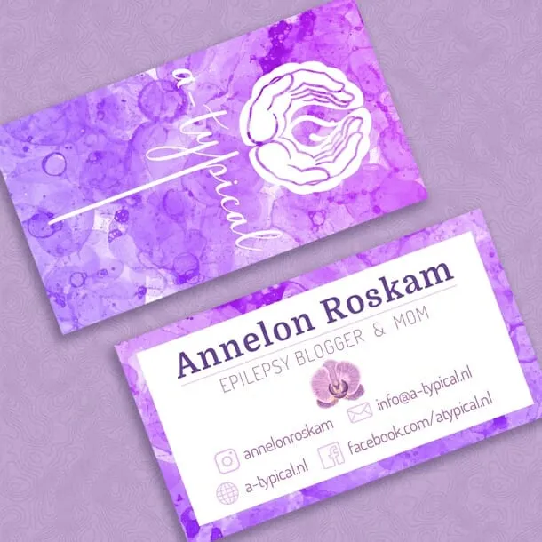 Two a-typical business cards on a lilac ground. The front is a purple watercolour wash carrying a white line mark of two cupped hands holding a flame, with the wordmark a-typical set vertically in white script; the back is white, with Annelon Roskam, epilepsy blogger & mom, above social and contact details and a small orchid.